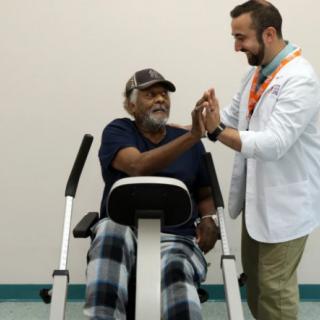 An elderly man receives encouragement from a healthcare professional during a physical therapy session.