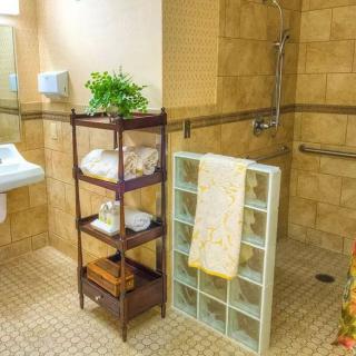 A well-organized bathroom with a wooden shelf holding towels and a plant, a tiled floor, and a walk-in shower area.