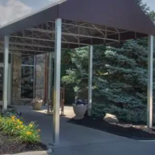 A covered entrance with a canopy surrounded by landscaping and trees.