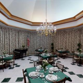 A sophisticated dining room with green tablecloths, elegant chandelier, and a piano in the corner.