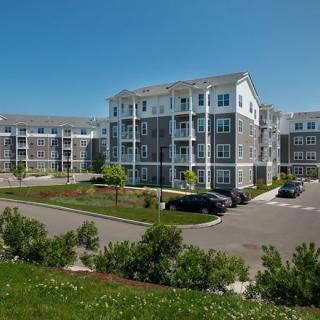 A modern apartment complex with landscaped surroundings and a parking lot under a clear blue sky.