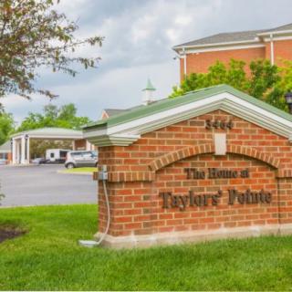 A brick sign at the entrance of a building with a parking lot in the background.