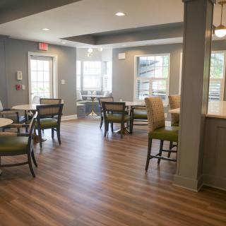 A cozy dining area with tables and chairs, featuring wood flooring and ample natural light from the windows.