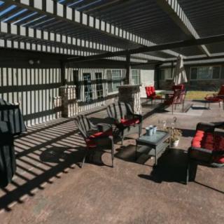A sunlit patio area with a pergola casting shadows over outdoor seating and furniture.