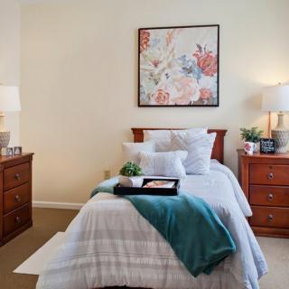 A cozy bedroom with a neatly made bed, wooden furniture, and soft lighting.