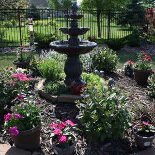 A beautifully landscaped garden featuring a decorative fountain surrounded by vibrant flowers and lush greenery.