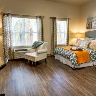 A cozy bedroom with natural light, featuring a stylish bed, patterned armchair, and elegant decor.