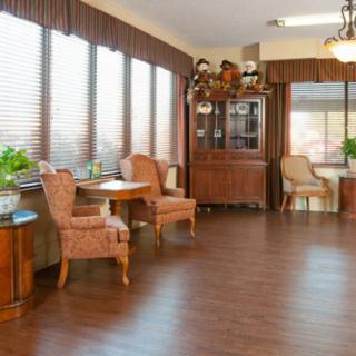 A cozy dining area with wooden floors, elegant furniture, large windows, and decorative plants.