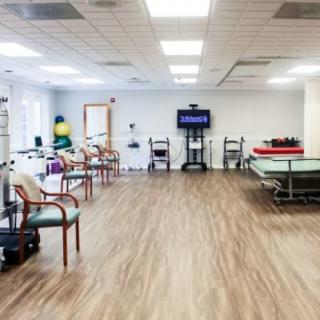 A spacious physical therapy room equipped with exercise equipment and chairs, designed for rehabilitation sessions.