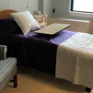 A cozy bedroom with a single bed, featuring a side table and chair next to a window.