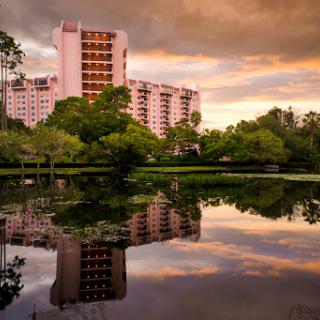 A serene view of a building reflecting on the water during sunset, surrounded by lush greenery.