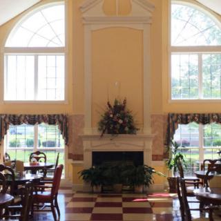 A bright dining room with large windows and classic decor, featuring a fireplace surrounded by tables and chairs.