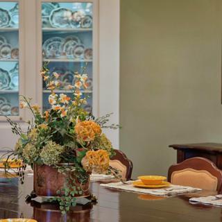 A beautifully set dining room table with a floral centerpiece and decorative china cabinet.