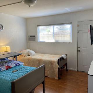 A bright bedroom featuring two single beds, a window, a lamp, and a wall-mounted TV.