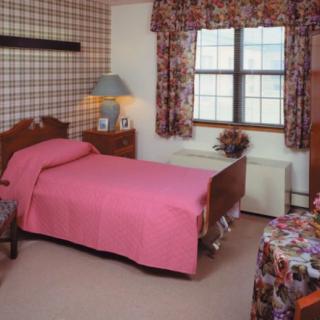 A vintage bedroom featuring a single bed with pink bedding, floral curtains, and wooden furniture.
