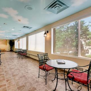 A cozy lounge area featuring tables and chairs, brightened by natural light streaming through large windows.