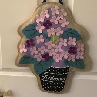 A decorative welcome sign featuring purple flowers in a pot.