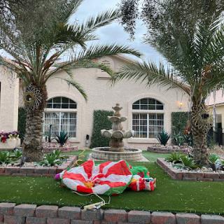 A beautifully landscaped yard featuring palm trees and a fountain, adorned with festive decorations.