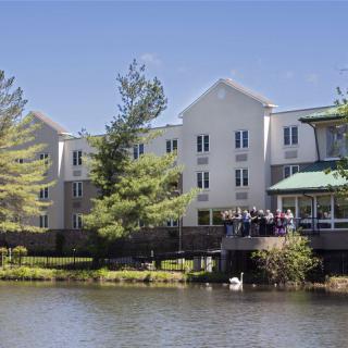 A scenic view of a building by the lakeside with surrounding trees under a clear blue sky.