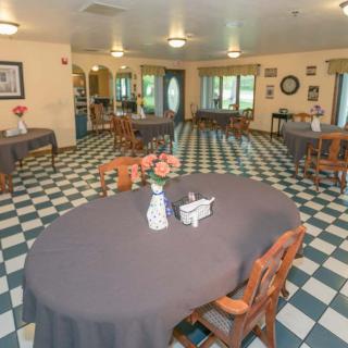 A spacious dining area with checkered floors, round tables draped in gray tablecloths, adorned with flowers.