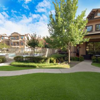 A scenic view of an apartment complex with a well-maintained lawn and trees on a sunny day.