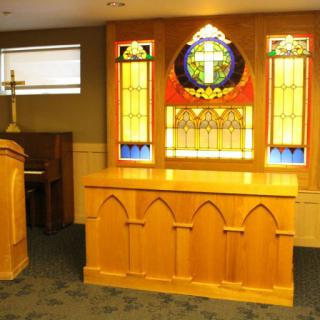 A church interior featuring an altar with stained glass windows and a cross.
