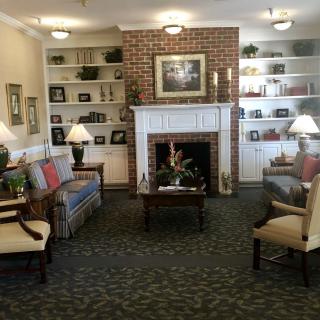 A cozy living room with a brick fireplace, comfortable seating, and decorative shelves.
