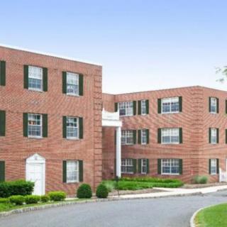 A brick apartment building with green shutters and well-kept landscaping.