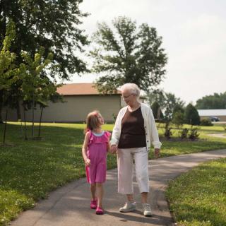An elderly woman and a young girl walking together in a park on a sunny day.