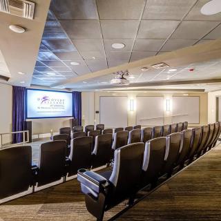 An empty theater with rows of seats facing a projection screen.