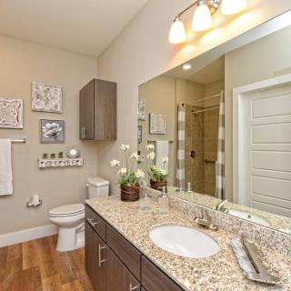 A modern bathroom interior featuring a granite countertop, large mirror, and contemporary lighting.