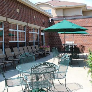 A sunny patio area with tables, chairs, and umbrellas next to a brick building.