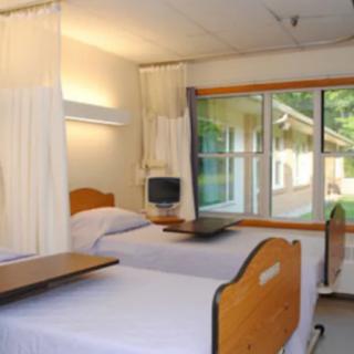 A hospital room with two patient beds and a window offering an outside view.