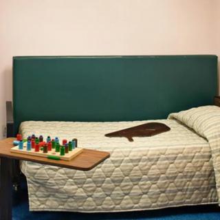 A bedroom with a quilted bedspread and a wooden tray holding colorful puzzle pieces.