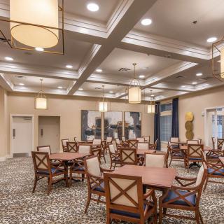 A spacious dining area with multiple tables and chairs, elegantly lit by ceiling lights.