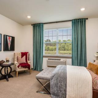A stylishly decorated bedroom with teal curtains, a comfortable bed, and framed artwork on the walls.