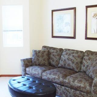 A cozy living room featuring a patterned sofa and an ottoman, plemented by framed wall art.