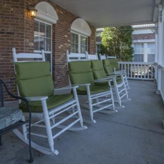 A row of white rocking chairs with green cushions on a covered porch.