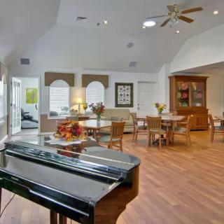 A spacious and well-lit living room featuring a piano, dining area, and wooden flooring.