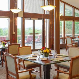 A bright and inviting restaurant interior with neatly set tables and large windows overlooking a scenic view.