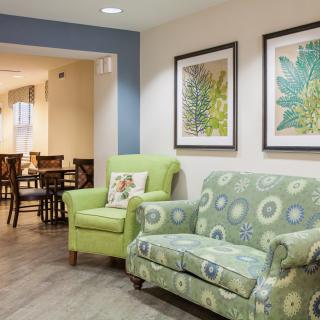 A cozy living room featuring a patterned sofa, a green armchair, and framed artwork on the walls.
