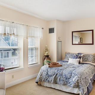 A cozy bedroom with a neatly made bed, large windows, and a wall mirror.