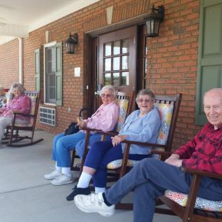 A group of elderly individuals relaxing on rocking chairs on a porch.