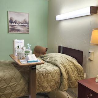 A neatly arranged hospital room featuring a patient bed, bedside table with medical supplies, and soft lighting.