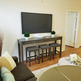 A modern living room with a mounted television above a console table and stools, accented by potted plants.