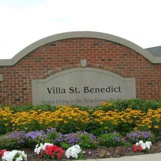 Entrance sign for Villa St. Benedict surrounded by colorful flowers.