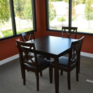A cozy dining area with a dark wooden table and four matching chairs, surrounded by large windows.