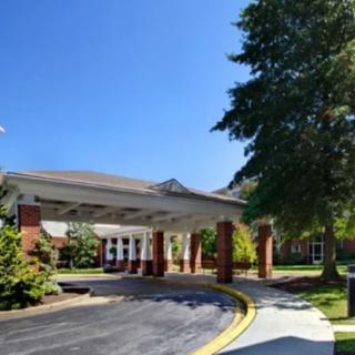 A building entrance with a covered driveway surrounded by trees on a sunny day.