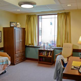 A cozy bedroom with a desk, wardrobe, and window with yellow curtains.