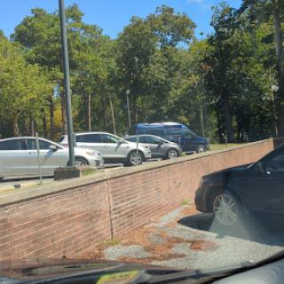 A view of a parking area with several cars surrounded by trees on a sunny day.